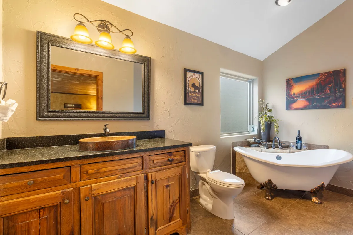 A spacious bathroom with a freestanding bathtub, granite countertop, wooden vanity, and a large mirror. The atmosphere is calm and spa-like, inviting guests to unwind after an active day.