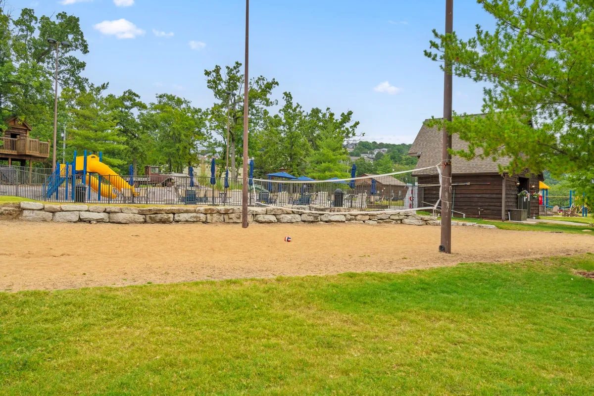 A lively playground scene with families and children enjoying colorful playground equipment, a sand volleyball court, and picnic areas nestled among trees. The image radiates joy and energetic social interaction, showing kids playing while adults relax and socialize nearby.