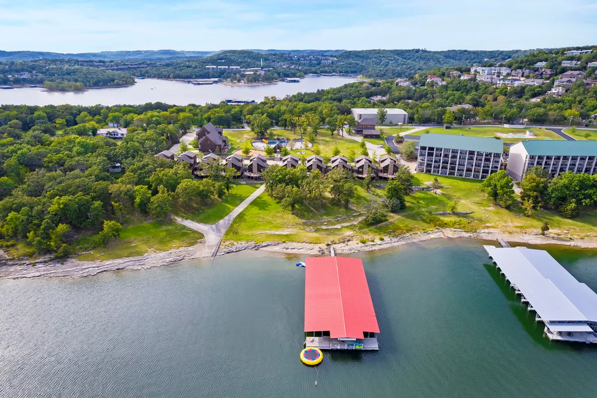 An expansive view of the lake, boathouse, dock, and resort buildings, all nestled amidst greenery. The scene evokes a sense of access to the lake, recreational possibilities, and the exclusivity of resort living.