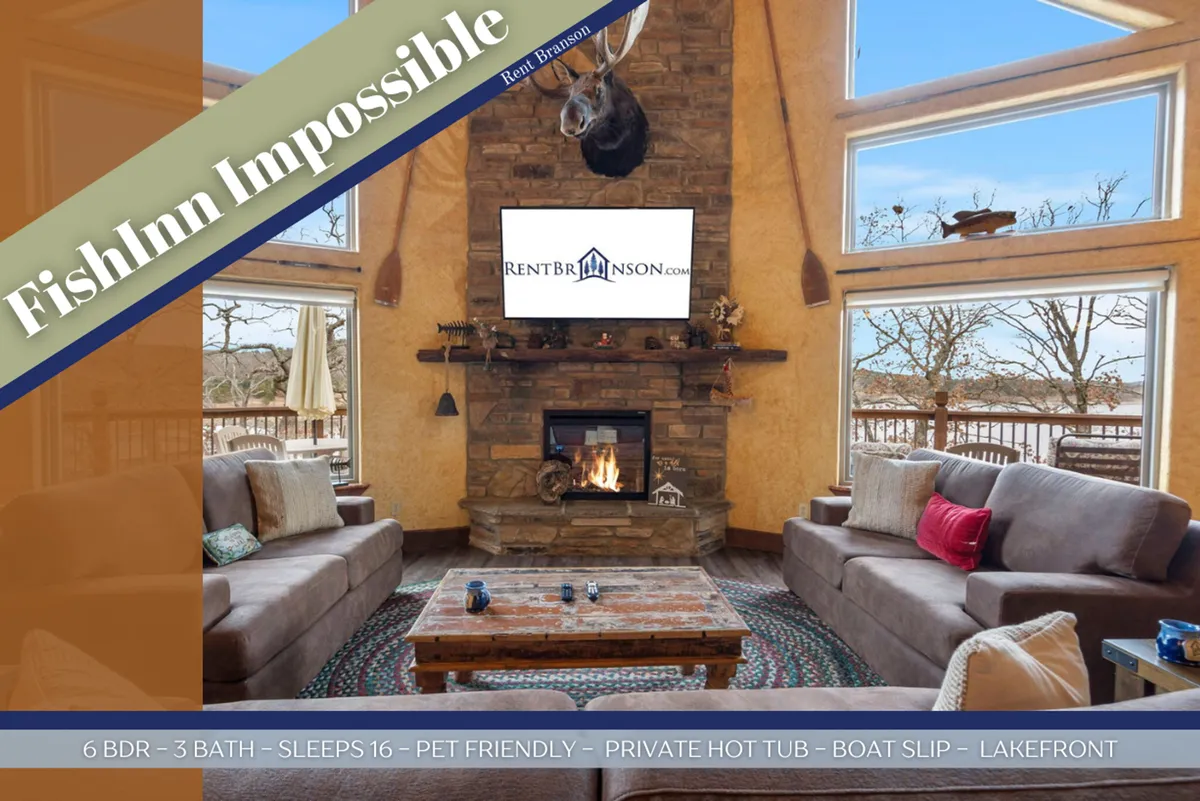 A spacious, comfortable lower-level living area with a large stone fireplace, abundant seating, a central coffee table, and expansive windows framing a lake view. The atmosphere is inviting and perfect for group gatherings.