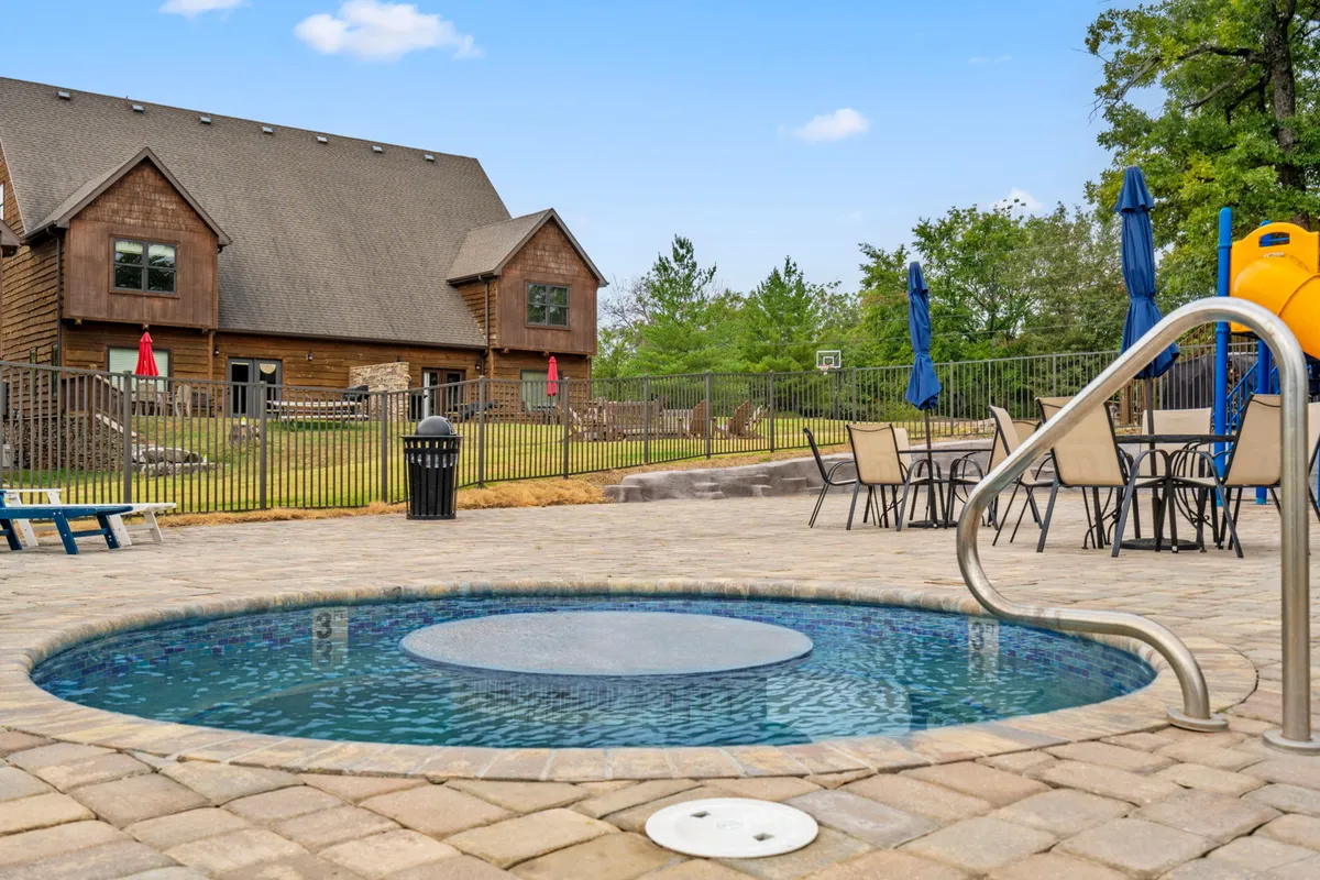 This image captures an inviting outdoor leisure area featuring a hot tub, swimming pool, picnic space, slide, and the exterior of the house. The hot tub is set against a scenic backdrop, ideal for relaxation, while the pool and picnic area highlight family-friendly amenities.