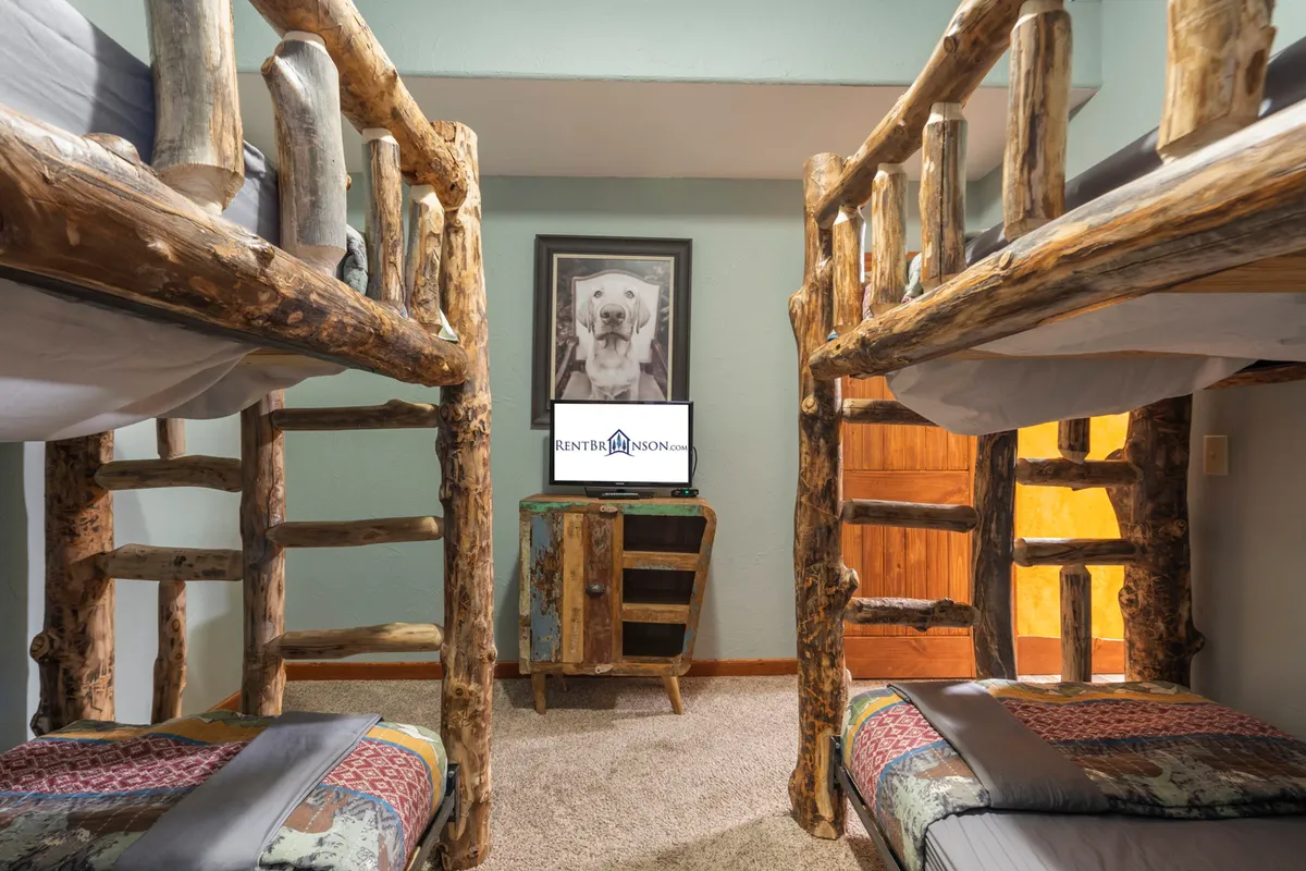 A playful bunk room is furnished with sturdy wooden bunk beds, a framed bear portrait, a TV, and additional wooden furniture. The room is cheerful and cozy, clearly intended for children or cousins to gather for fun sleepovers.