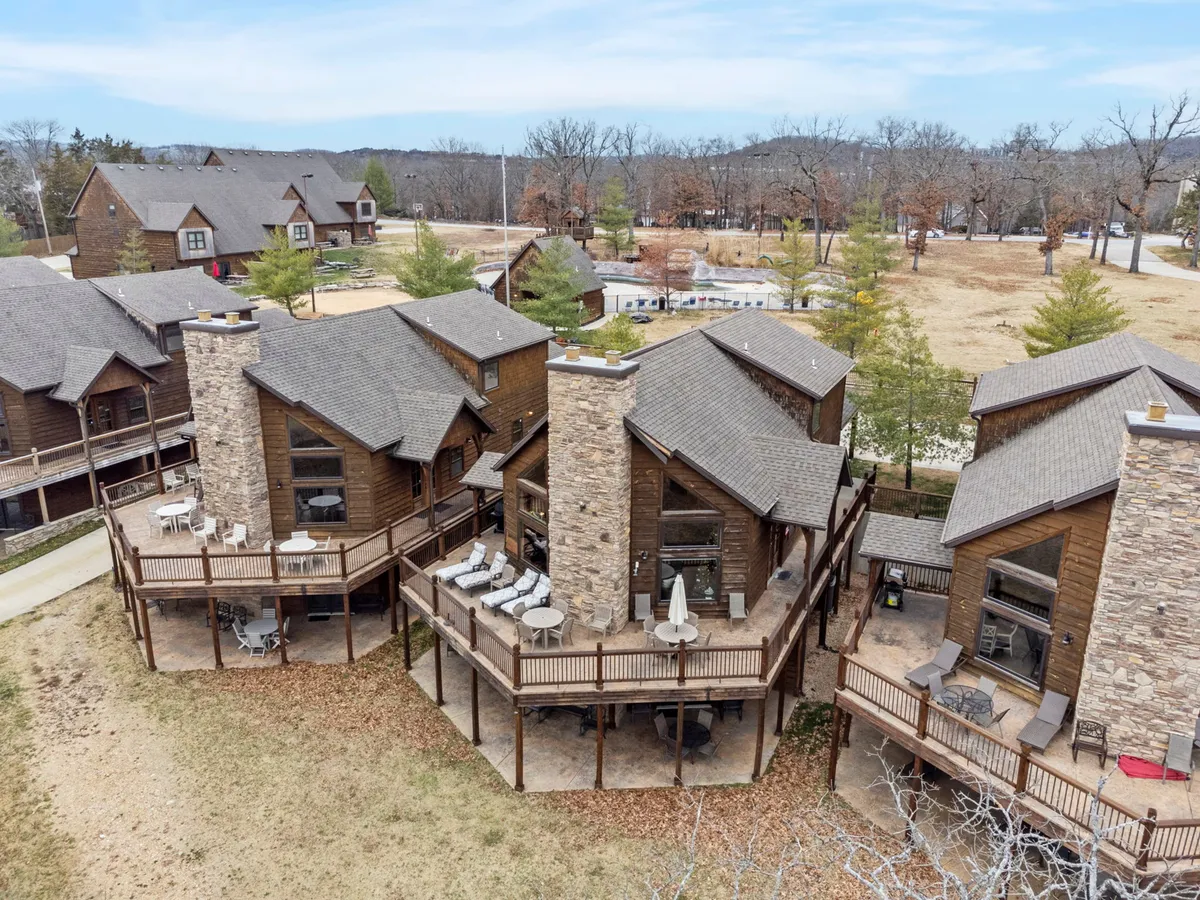 A cluster of wooden cabins with stone chimneys and outdoor seating areas, surrounded by landscaped greenery. Decks offer ample space for lounging, and the atmosphere is rustic and cozy, seamlessly blending with the outdoors.