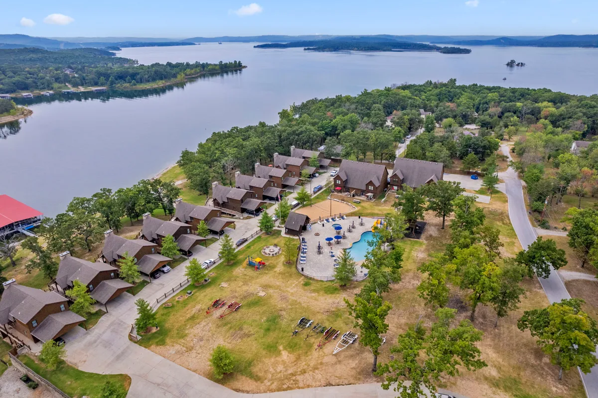 A wide shot showcasing the lake, swimming pool, nearby cabins, and a dedicated play area. The scene features families swimming, boating, and engaging in nature walks along the shoreline, with sunset lighting enhancing the recreational, family-friendly atmosphere.