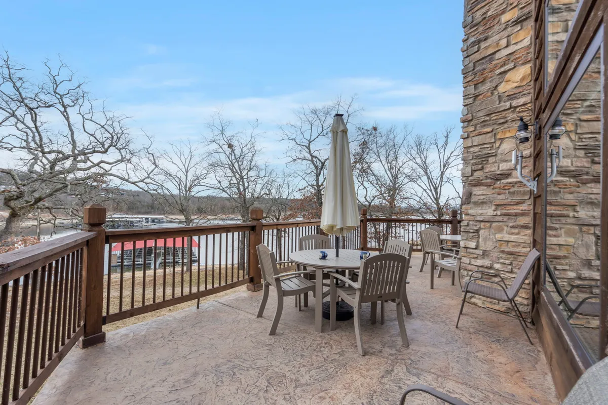 An inviting exterior scene with a dining table and umbrella overlooking the water. The table is set for outdoor dining, and the tranquil lake view creates a peaceful atmosphere ideal for morning coffee or sunset gatherings.
