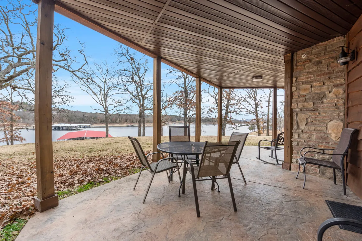 A peaceful patio setting with a table and chairs overlooks the serene lake and is surrounded by tall trees. The scene is tranquil, perfect for quiet outdoor meals, morning coffee, or stretching while enjoying lake breezes.